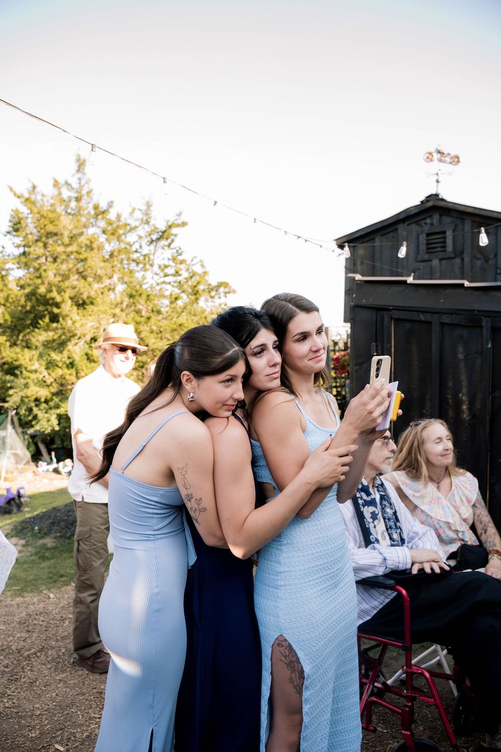 Group of wedding guests in light blue dresses gathered outside taking photos.
