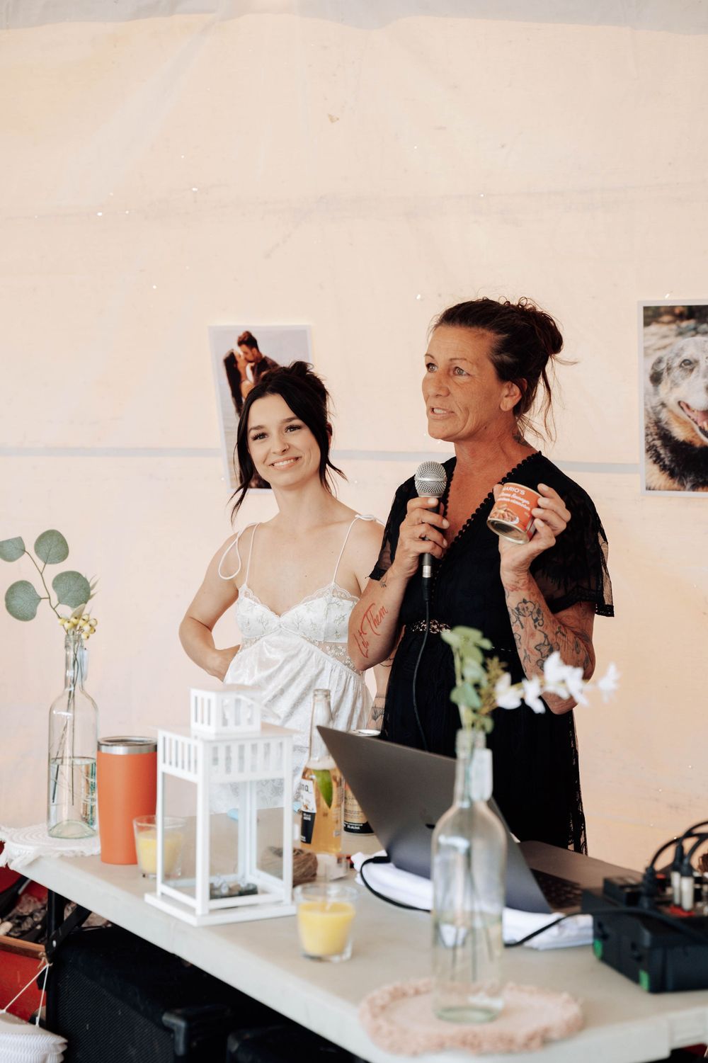 Two wedding vendors in casual attire stand behind a table with decorative lanterns and bottles.