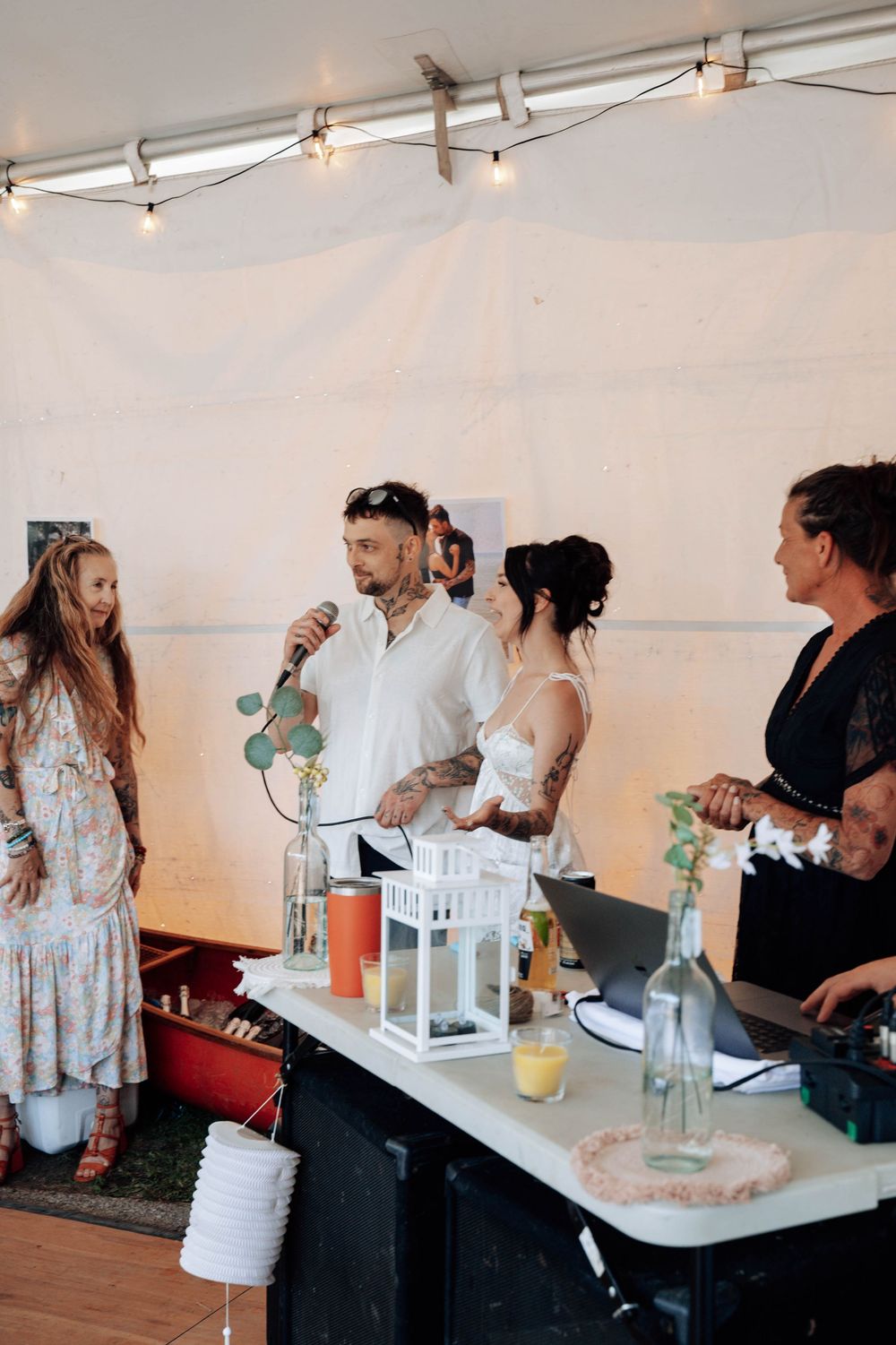 Wedding reception guests mingling under a white tent with string lights and refreshment tables.