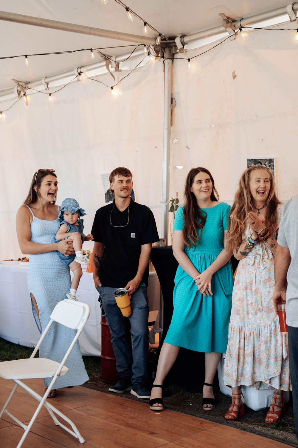 Group of guests enjoy a casual moment under a white tent at an outdoor celebration.