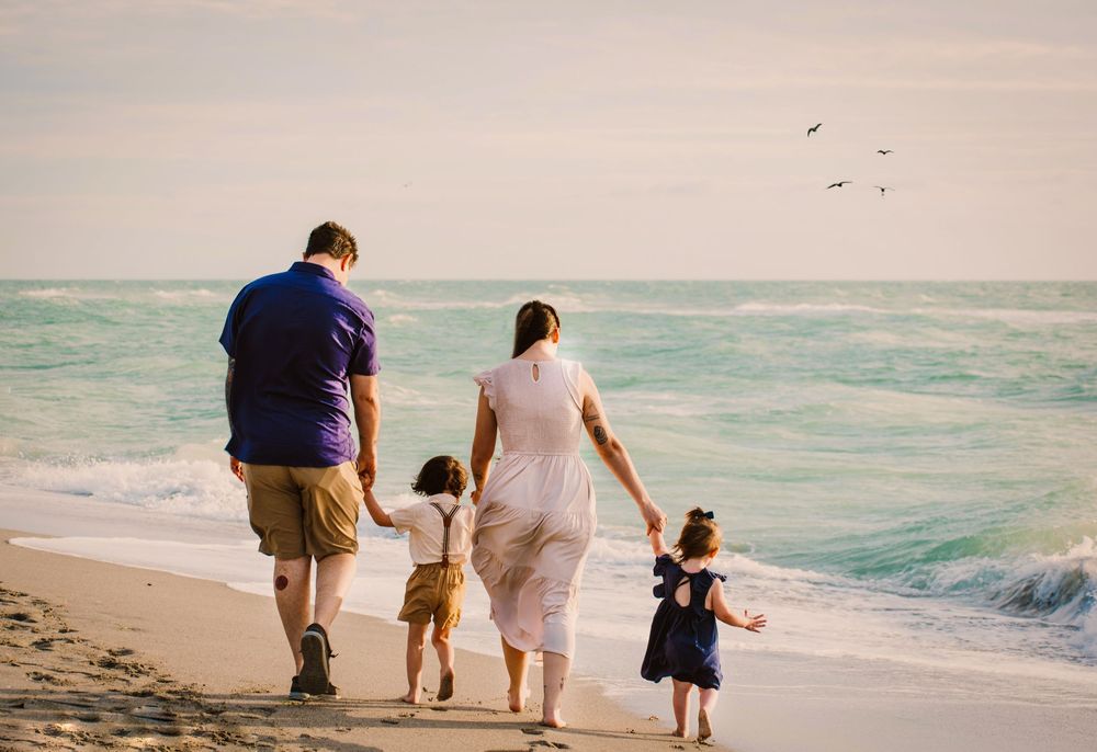 Family of four walking hand in hand down the beach during sunset lifestyle session.