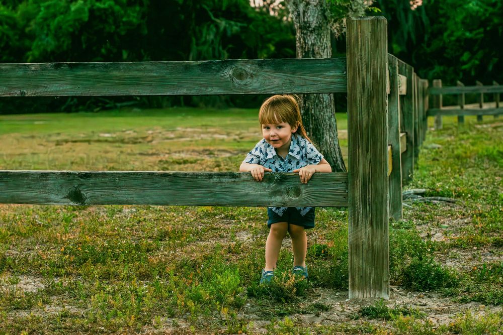Candid photo of toddler hanging on a wooden fence during outdoor lifestyle session.