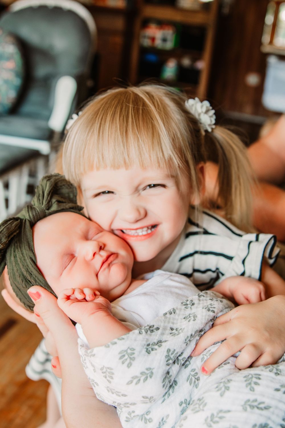 Toddler girl cradling newborn sister in natural light family photo.