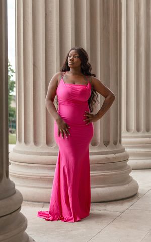 A woman in a flowing hot pink dress poses gracefully between classical stone columns in an elegant architectural setting.