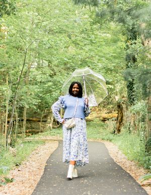 A person walking on a tree-lined path wearing a blue and white dress and holding a white umbrella.