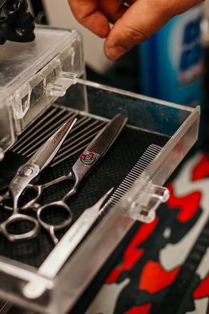 Professional barber scissors and grooming tools organized in a clear storage case on a patterned surface.