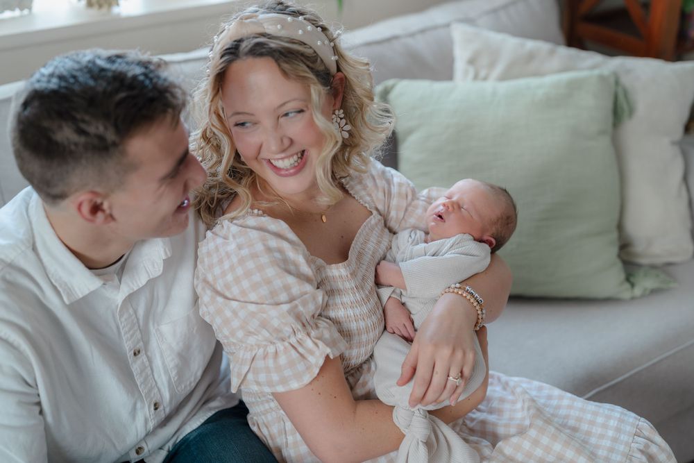 A heartwarming family moment shows parents sharing tender moments with their newborn baby on a light-colored couch in Cuyahoga Falls, Ohio