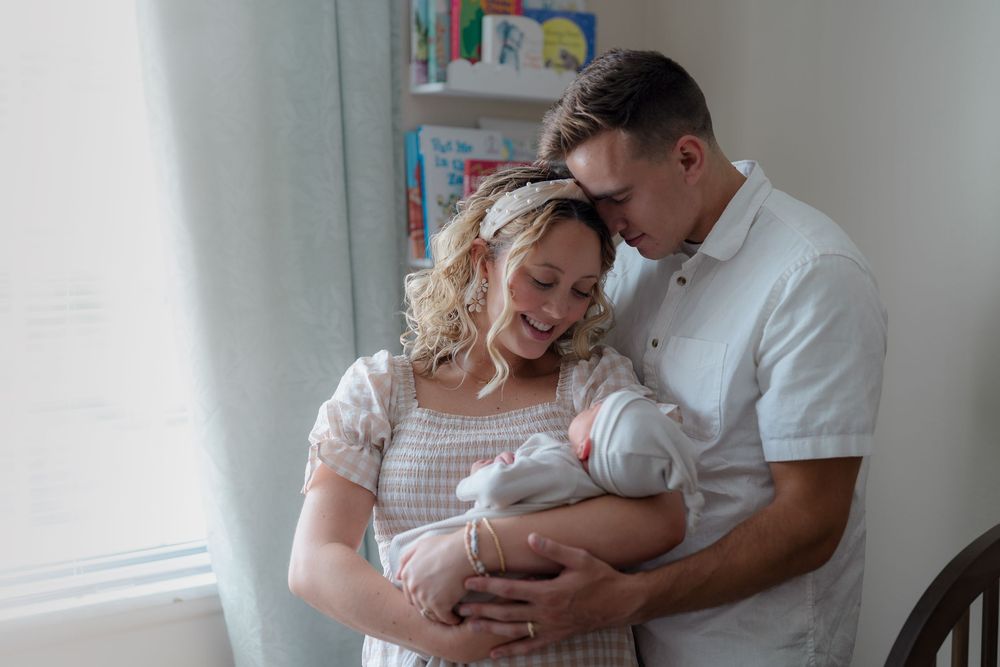 Parents share an intimate moment with their newborn baby in a cozy nursery corner with natural lighting in newborn photography session Ohio