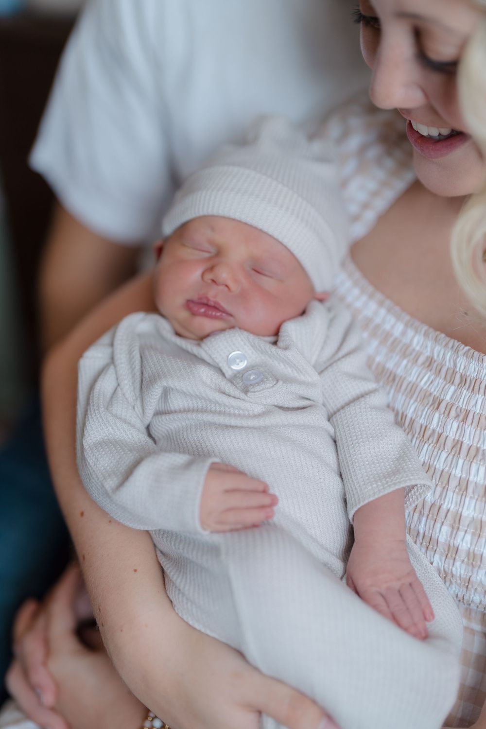 A newborn baby wearing a white knit outfit and hat sleeps peacefully in a cradled hold for newborn session in Cuyahoga Falls, Ohio