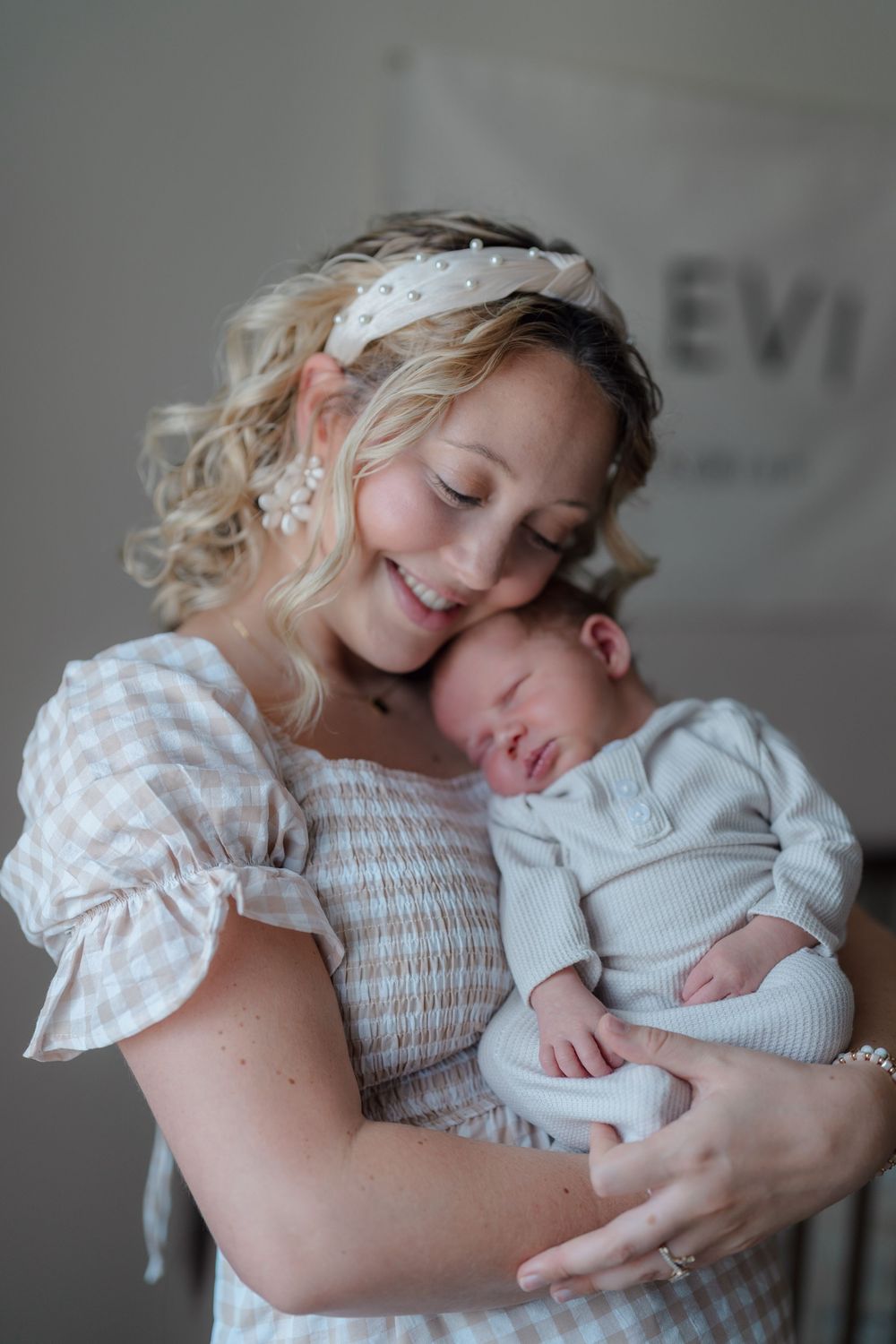 Tender moment captured as parent in white dress holds sleeping baby wearing light gray outfit at in-home newborn session, Cuyahoga Falls, OH
