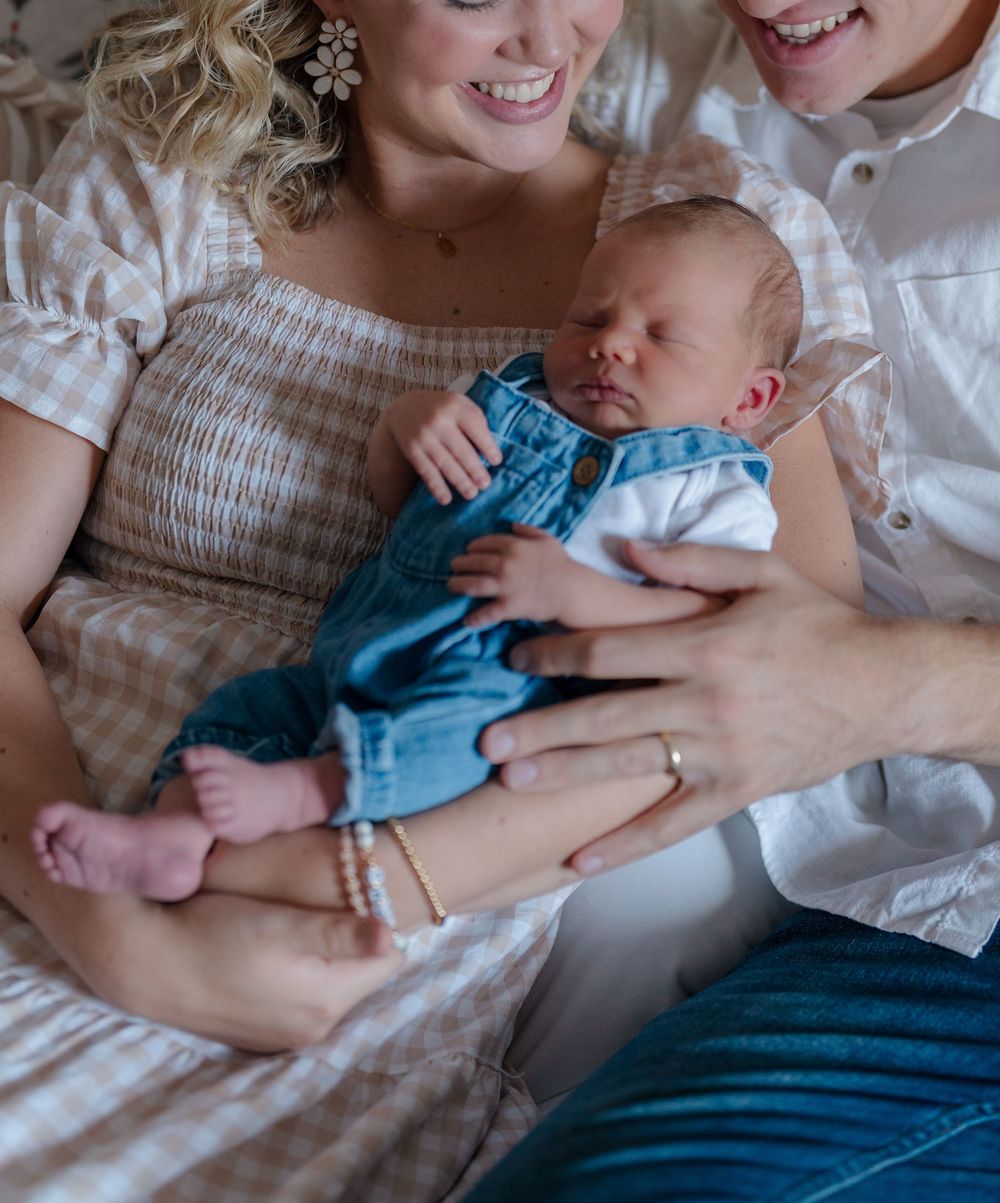 Sleeping newborn baby in denim overalls nestles peacefully in loving arms on white bedding at in-home newborn session near Stow, Ohio