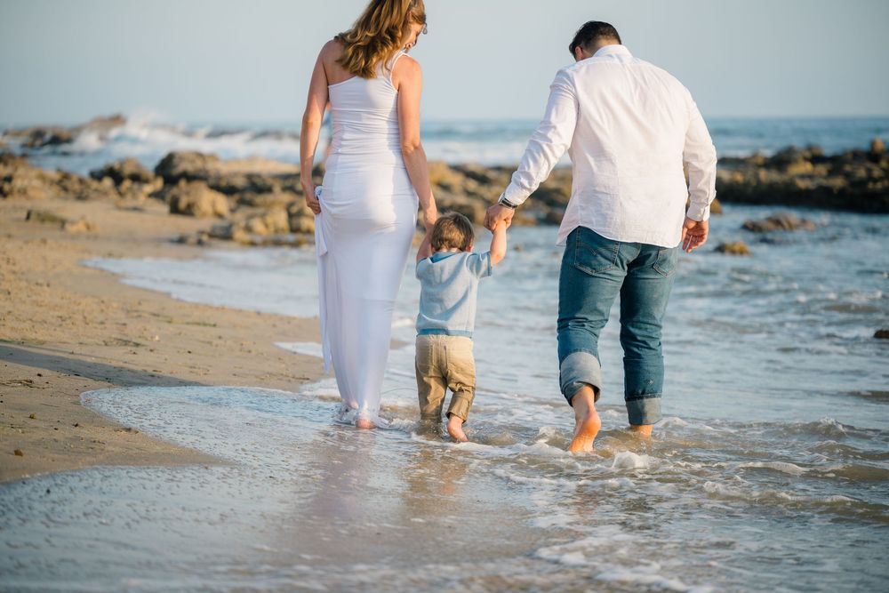 Family walks along shoreline of Newport Beach in white outfits in Orange County at sunset for photography session.
