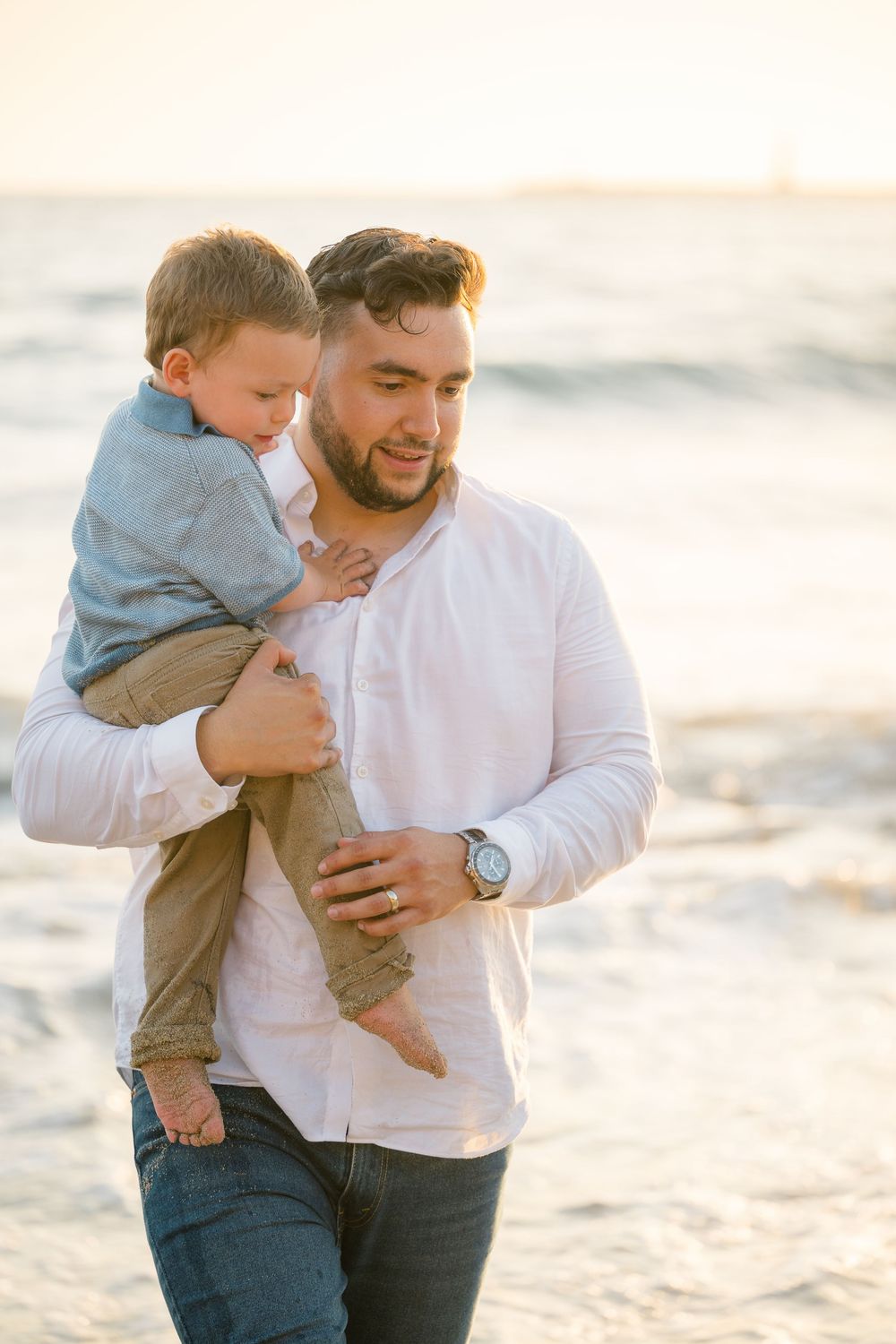 Father carries his toddler son in the ocean during a Newport Beach family photoshoot at sunset.