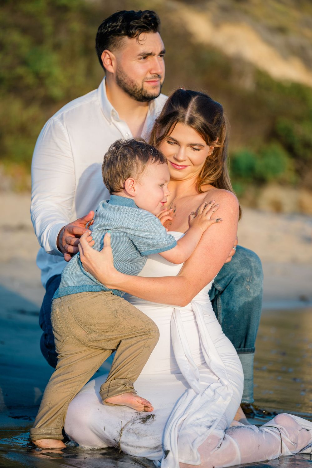 Luxury photography session in Orange County of family wearing white, blue and tan sitting on shore of Newport Beach.