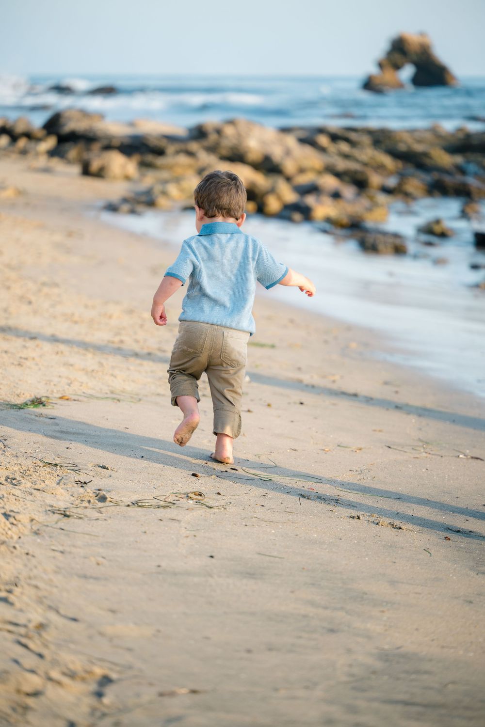 Toddler runs barefoot along the sandy shore during a Newport Beach family photo session in Orange County.