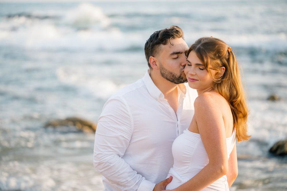 Expecting couple shares a gentle kiss by the Pacific Ocean during their Newport Beach maternity photoshoot.