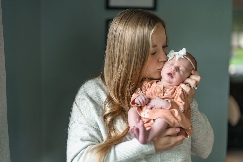 A tender moment between mother and newborn baby wearing pink as they snuggle close together indoors in Cuyahoga Falls, Ohio Newborn Session.