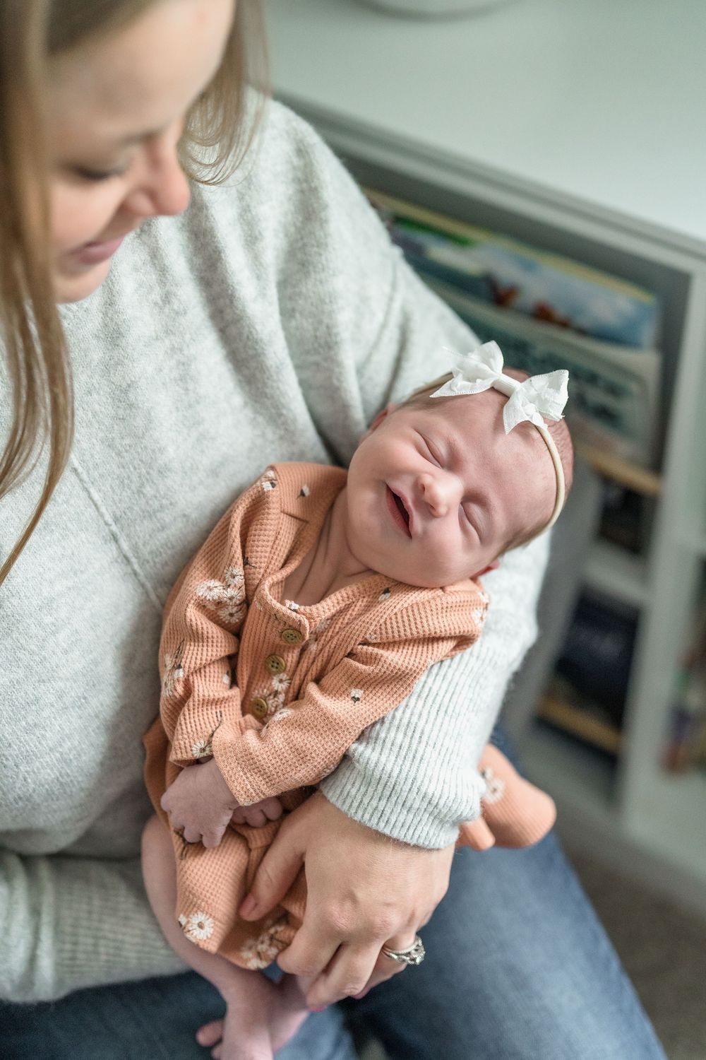 A sleeping newborn baby wearing a peach-colored knit outfit and white bow headband rests in mom's arms during newborn session in Ohio