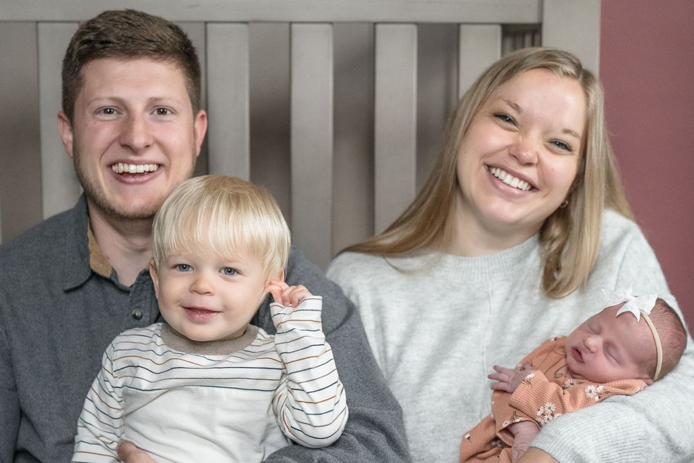 A happy family portrait featuring parents with their toddler and newborn baby at home in Cuyahoga Falls, Ohio Newborn Family Photo Session