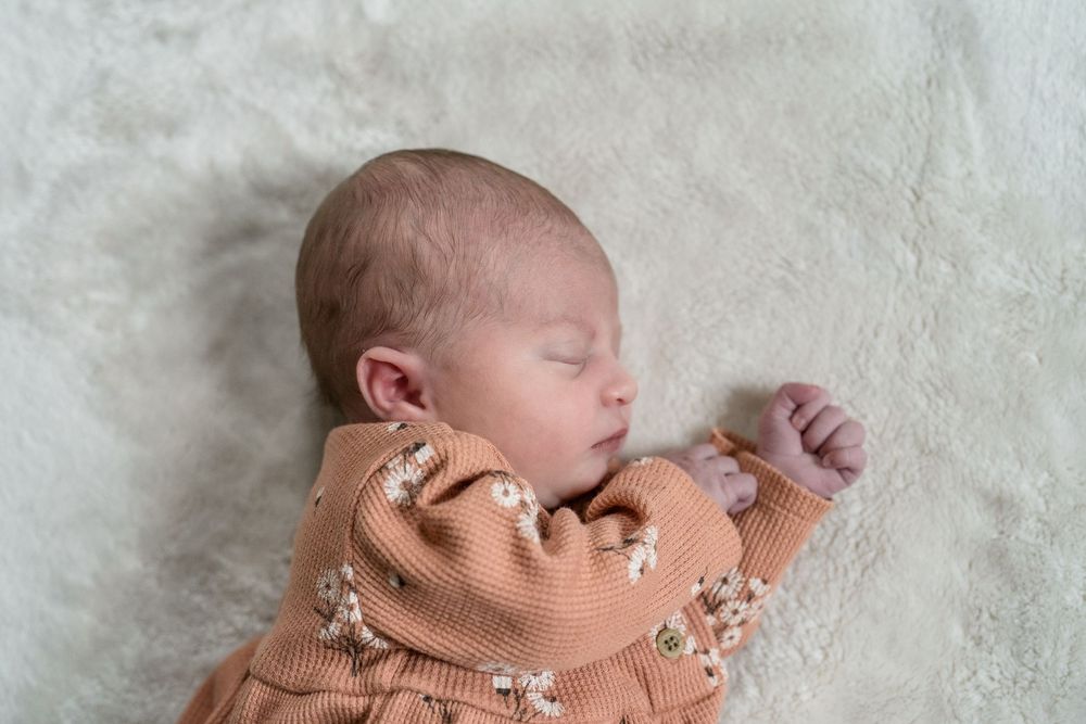 Peaceful sleeping newborn in tan floral sleepwear resting on white textured blanket at Cuyahoga Falls, Ohio Newborn Session