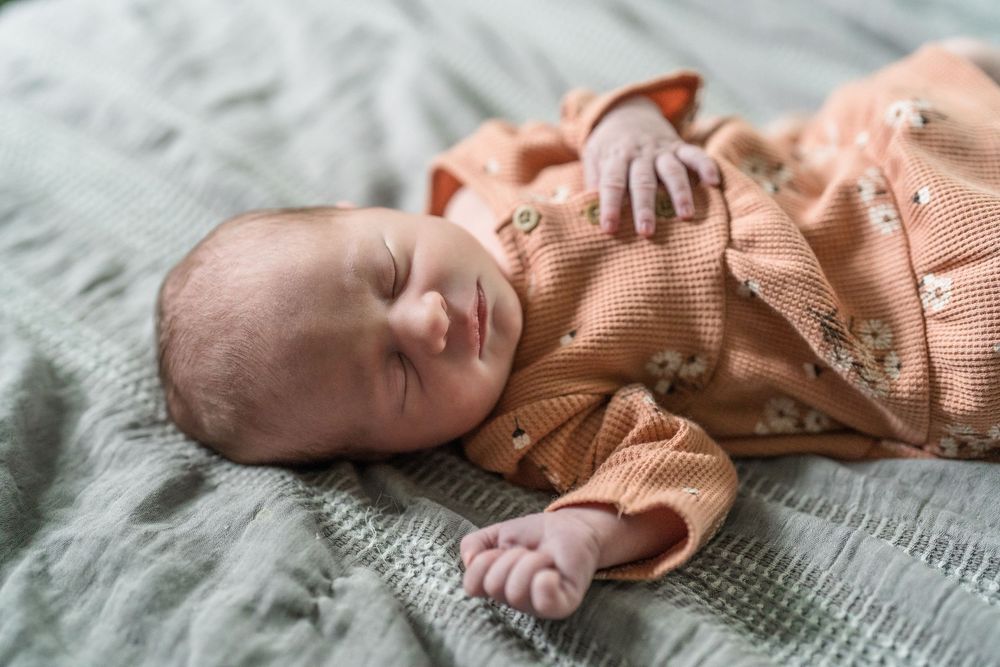 Baby sleeping peacefully on gray blanket wearing coral-colored knit cardigan outfit for a newborn session in Cuyahoga Falls, Ohio Family Pic