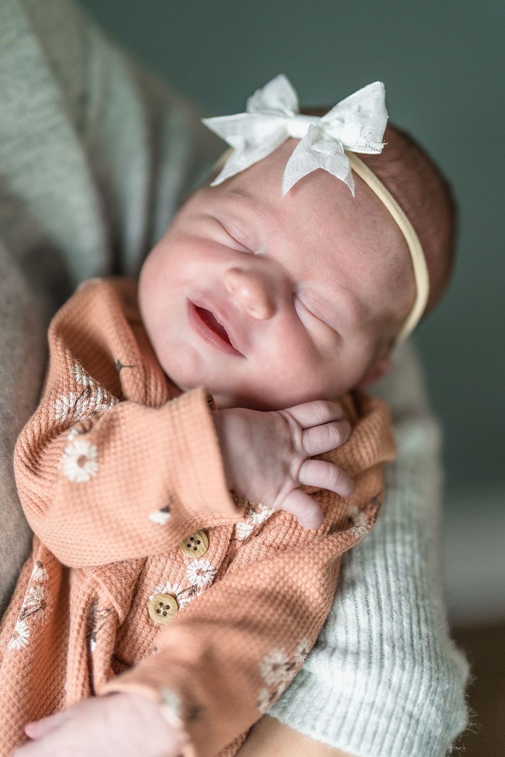 Sleeping newborn wearing peach colored cardigan and white bow headband smiles peacefully at home in Cuyahoga Falls, Ohio Newborn Session.