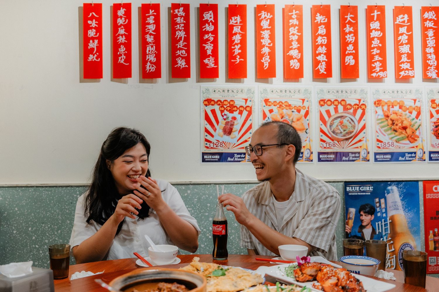 Two people enjoying a meal together at an Asian restaurant with traditional red banners and posters on the wall.