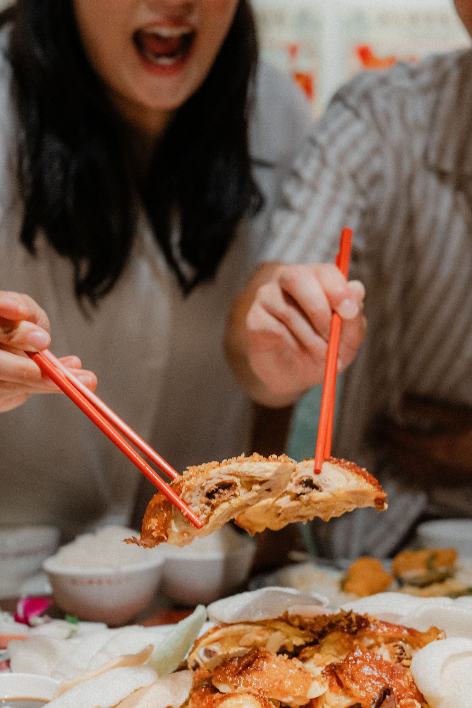 People using red chopsticks to pick up pieces from a shared seafood meal spread on a white table.
