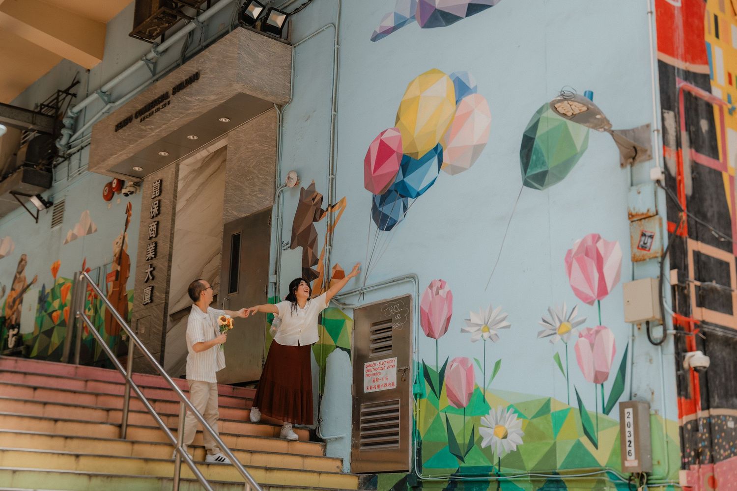 A colorful wall mural featuring bright pink tulips and flying birds decorates the side of a building near a staircase.