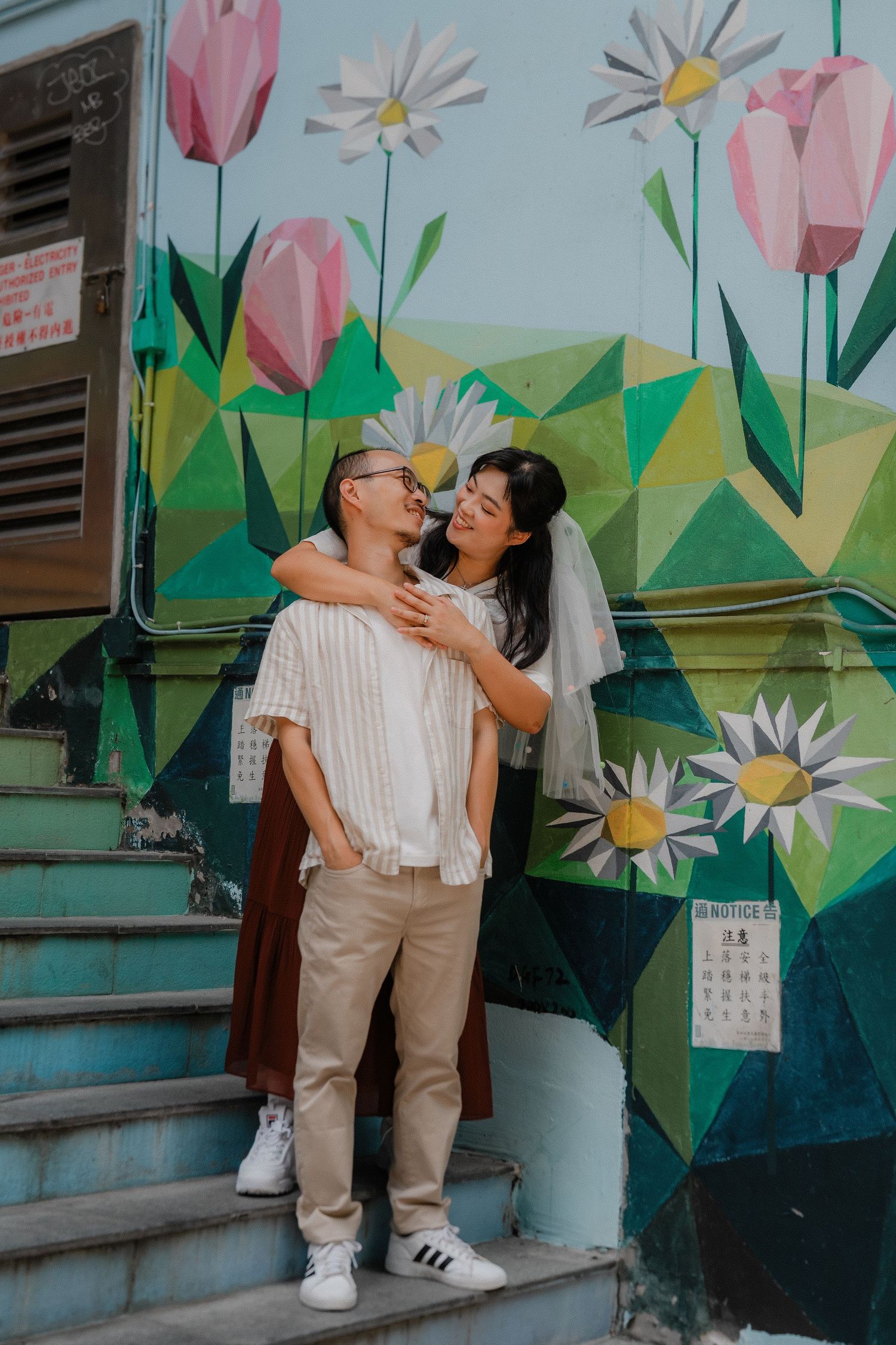 A couple shares a tender kiss on concrete steps against a wall with colorful floral mural artwork featuring tulips and daisies.