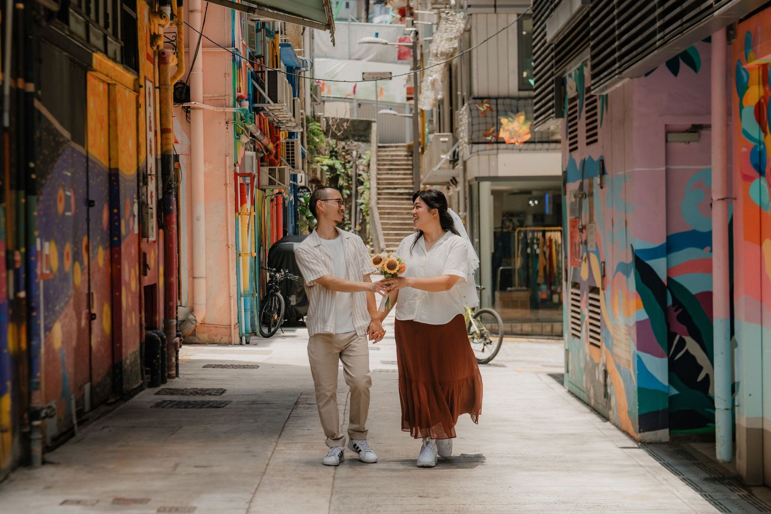 Two people walk together and chat while strolling down a colorful alleyway with painted walls in Singapore.