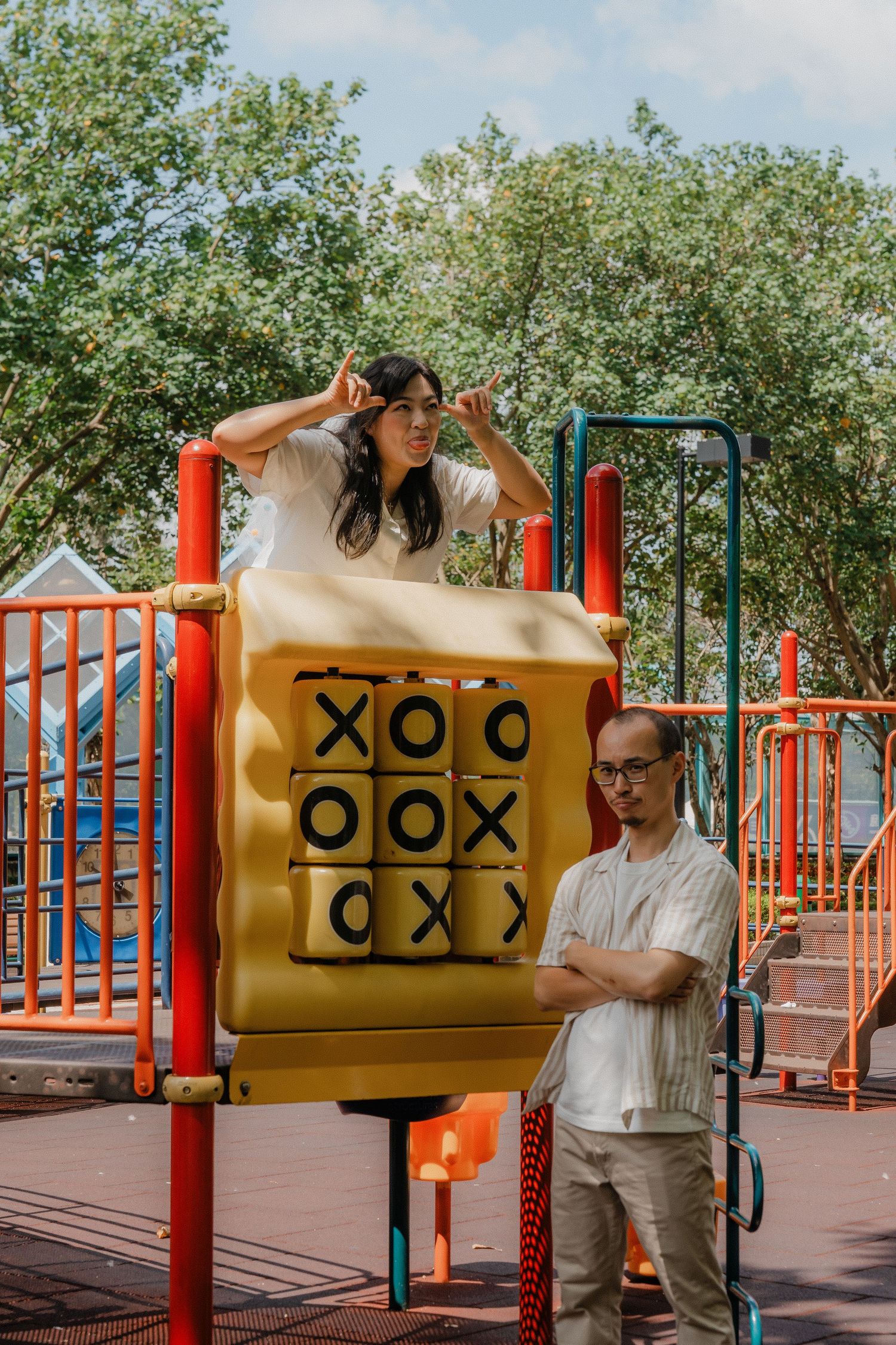 Fun capture at a playground with two people playing at a large yellow tic-tac-toe board on red climbing equipment.