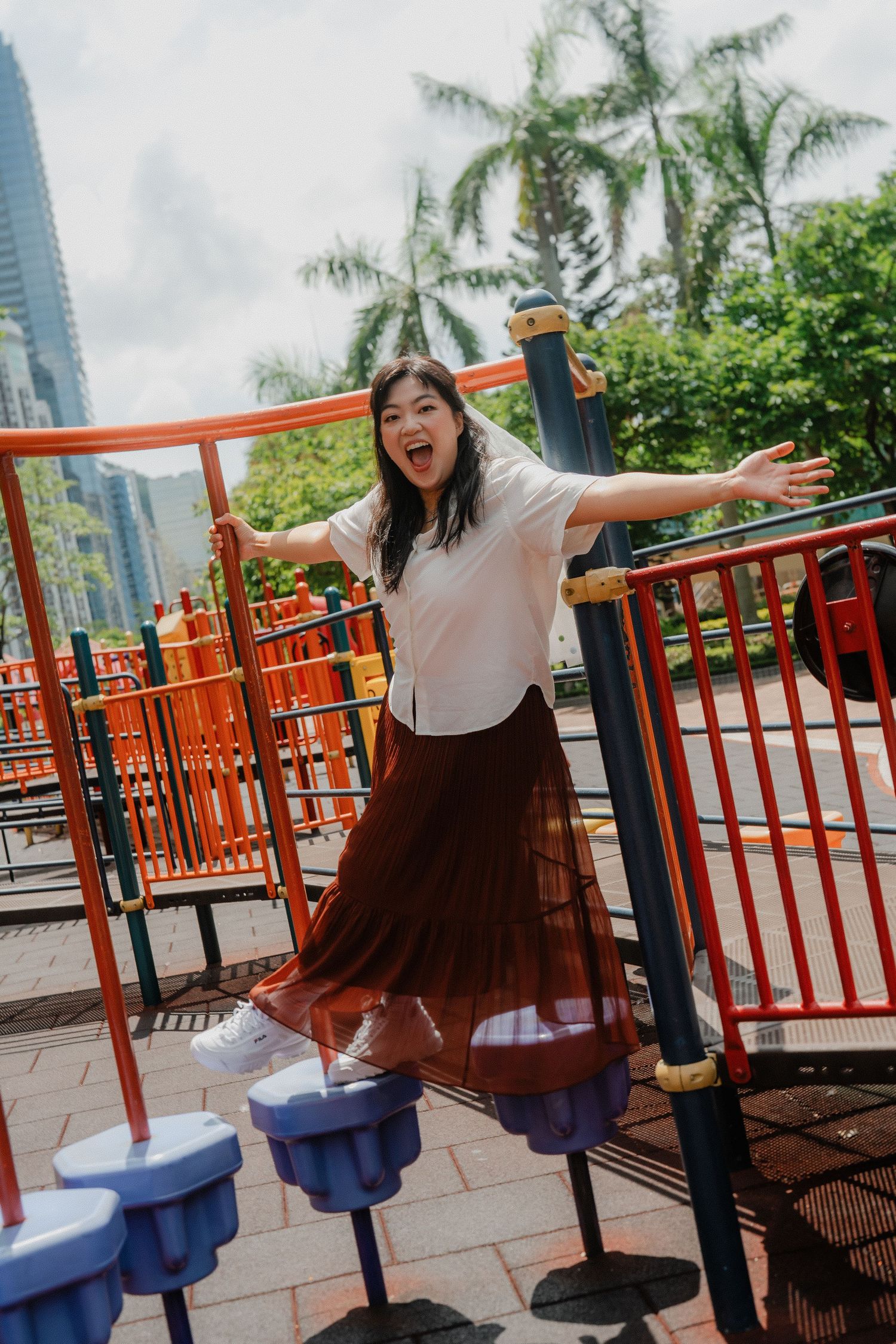 Someone wearing a white top and brown skirt plays on colorful stepping platforms at an outdoor playground area.
