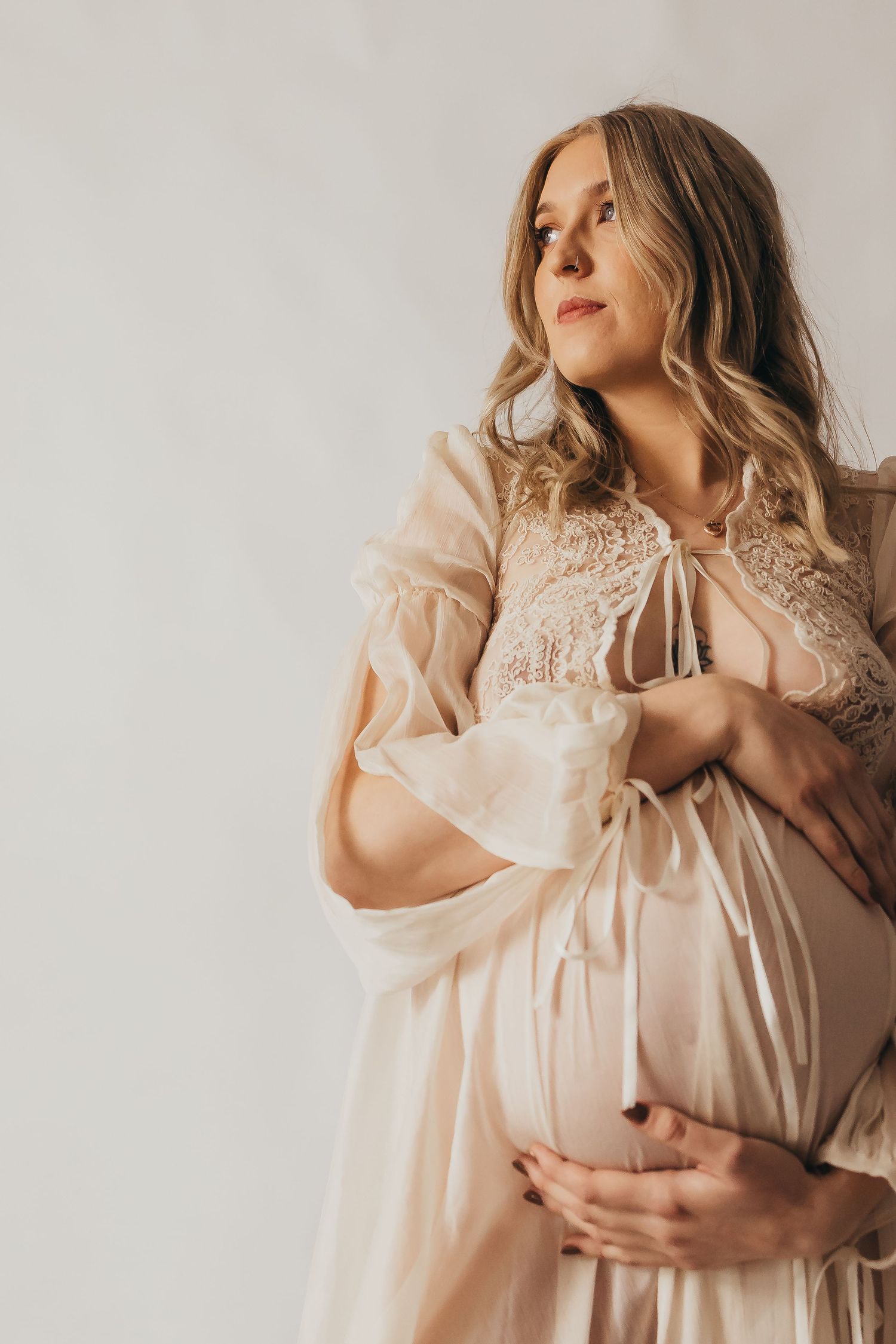 Romantic soft portrait in peach-colored vintage lace dress with flowing sleeves against light background.