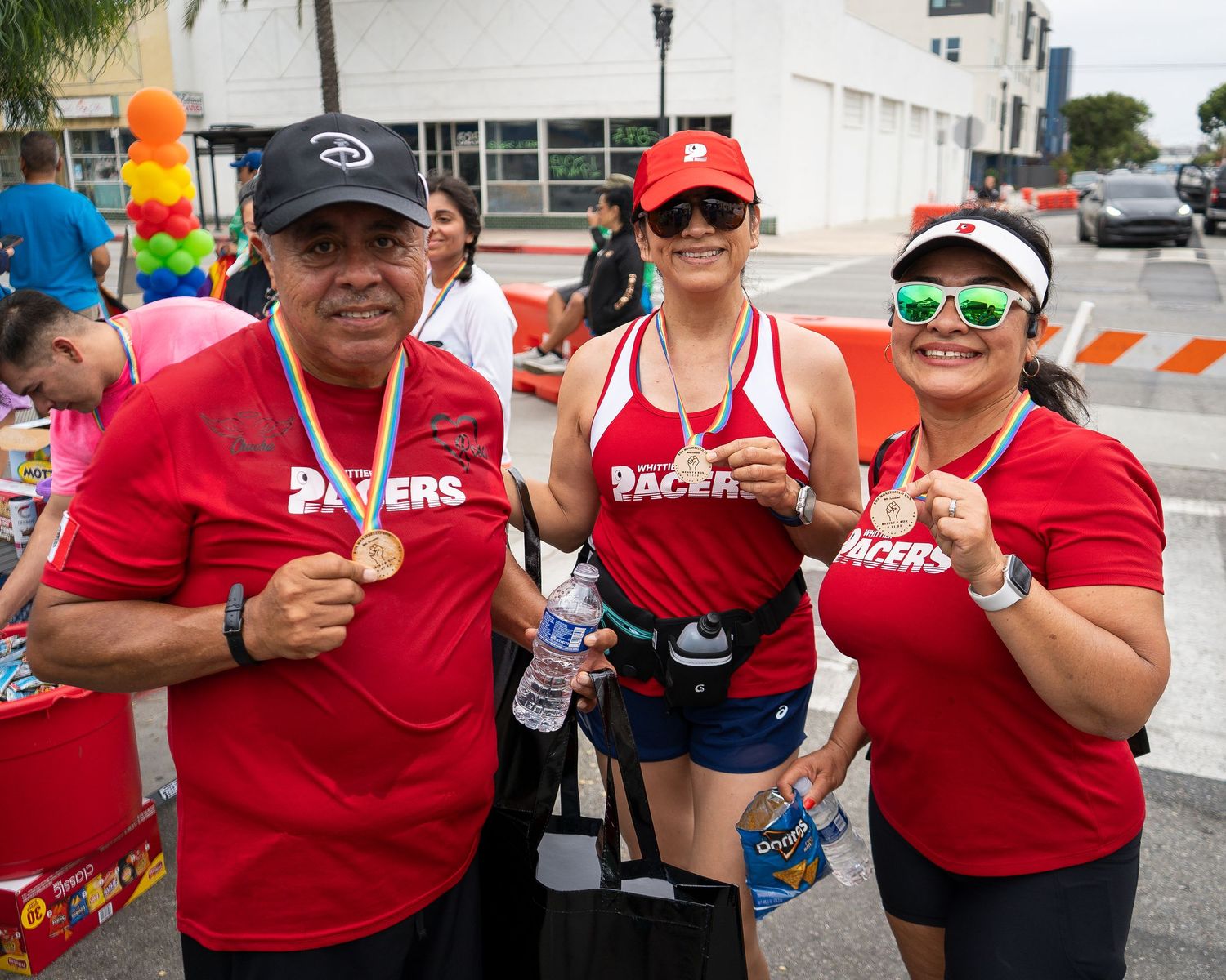 Three runners in red “Pacers” shirts show off medals after a race at a street event.