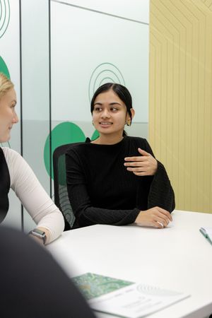 Two people having a conversation during a business meeting at a white table with papers visible.