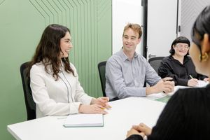 Colleagues engaged in discussion at a meeting table with a minimalist green wall backdrop.