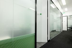A modern office hallway with frosted glass walls and doors showcasing a minimalist corporate interior design.