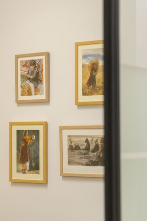 Gallery wall with framed artwork displayed in gold frames against a white wall divided by black vertical beams.