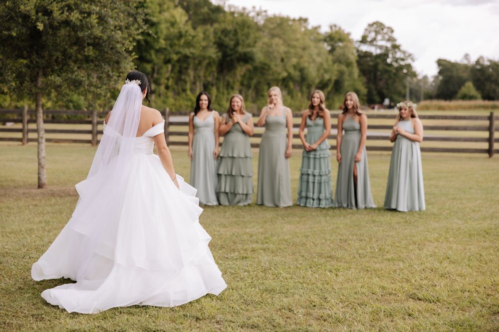 A wedding celebration in a rustic outdoor setting with sage green bridesmaid dresses and flowing white gown details.