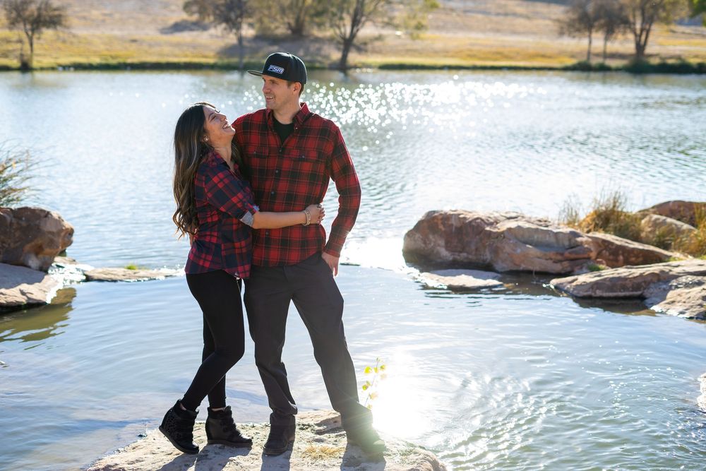 Couple in casual clothes embracing by a scenic lake with rocks and reflective water.  alt="Professional photography in Lubbock TX by H & Co.