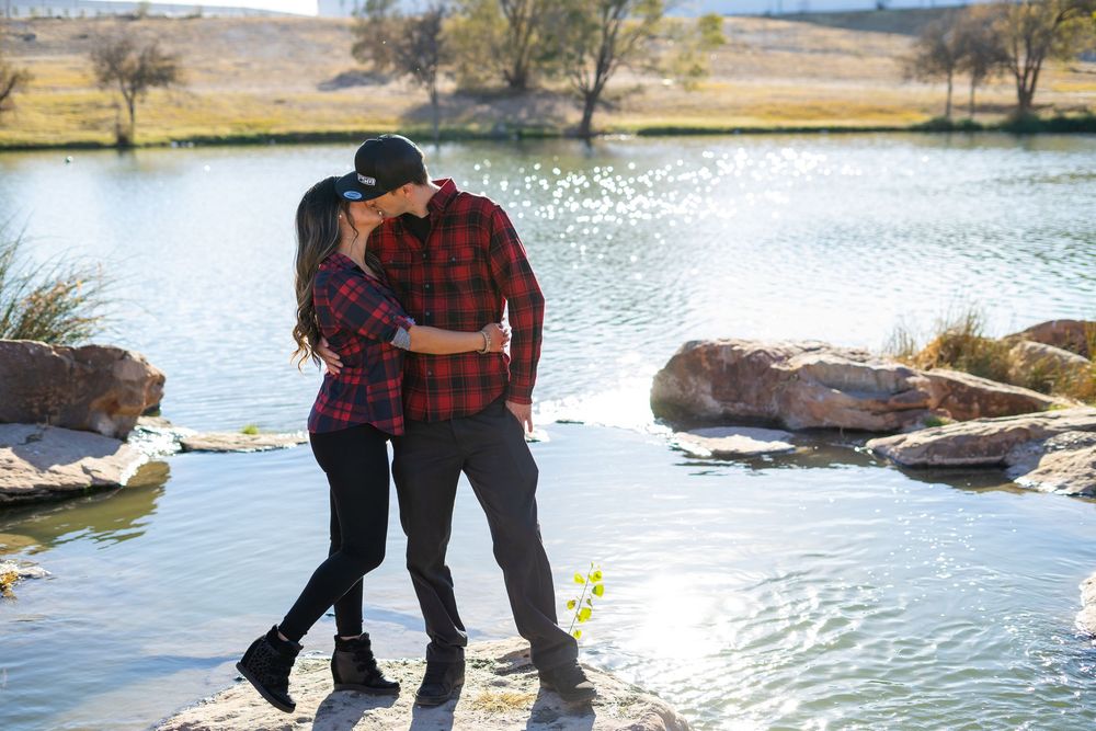 Romantic couple standing together on rocks by a serene lake during golden hour.
