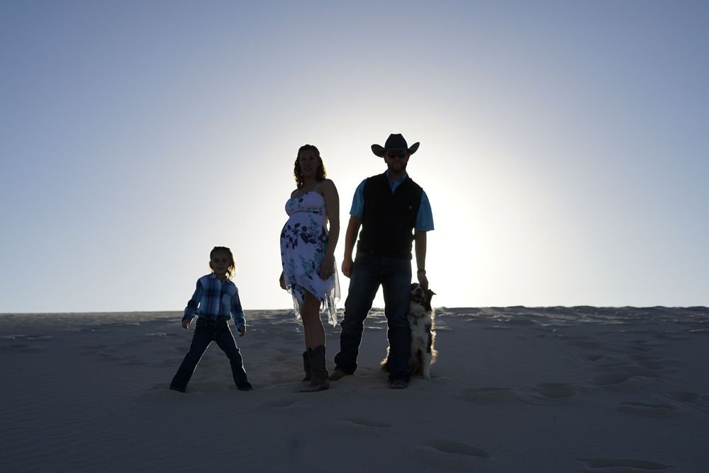 Dark silhouettes of a small group walking along a horizon at dusk. alt="Professional maternity photography in Lubbock TX by H & Co. Creative