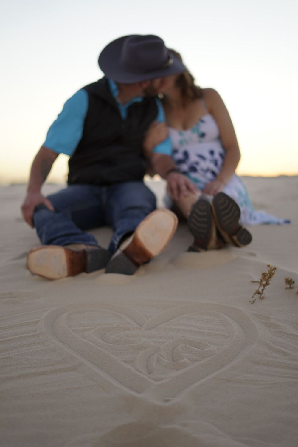 People drawing patterns and shapes in beach sand during sunset. alt="Professional maternity photography in Lubbock TX by H & Co. Creative