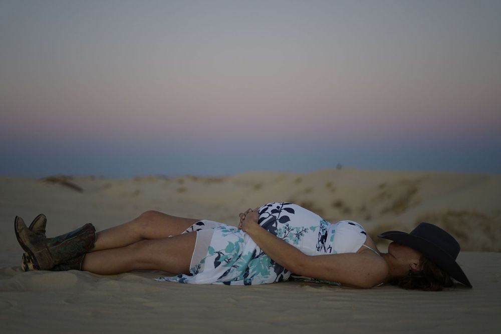 People relaxing on sandy dunes during a peaceful evening. alt="Professional maternity  photography in Lubbock TX by H & Co. Creative
