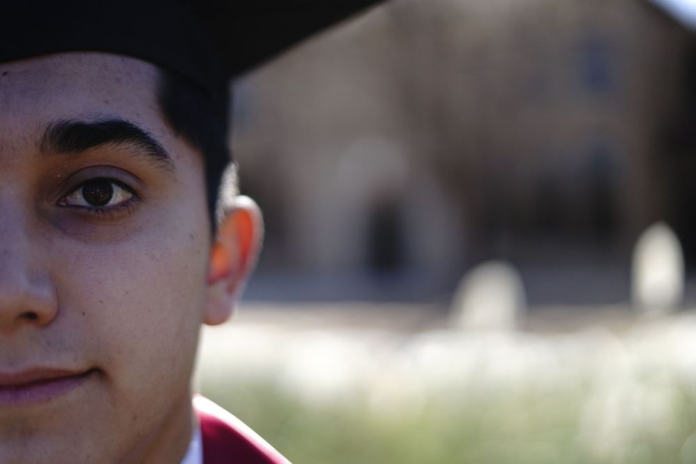 Graduate in red academic regalia poses outdoors with a blurred stone building in the background alt="Professional photography in Lubbock TX