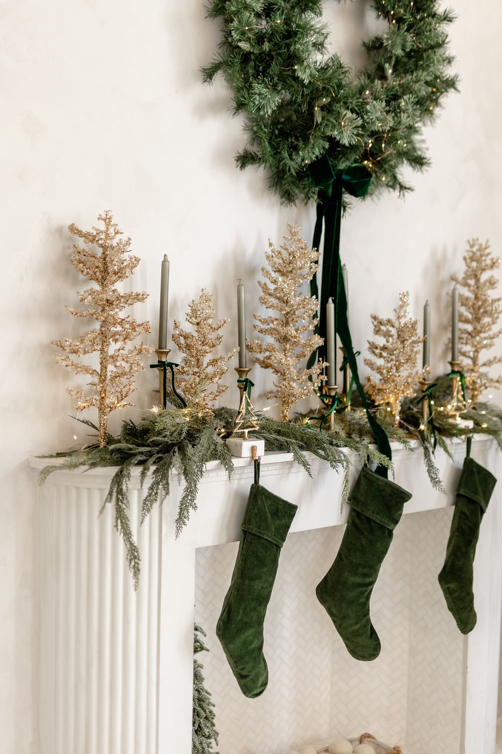 Green and white Christmas stockings hang from railing with evergreen garland and holiday decor against white wall.