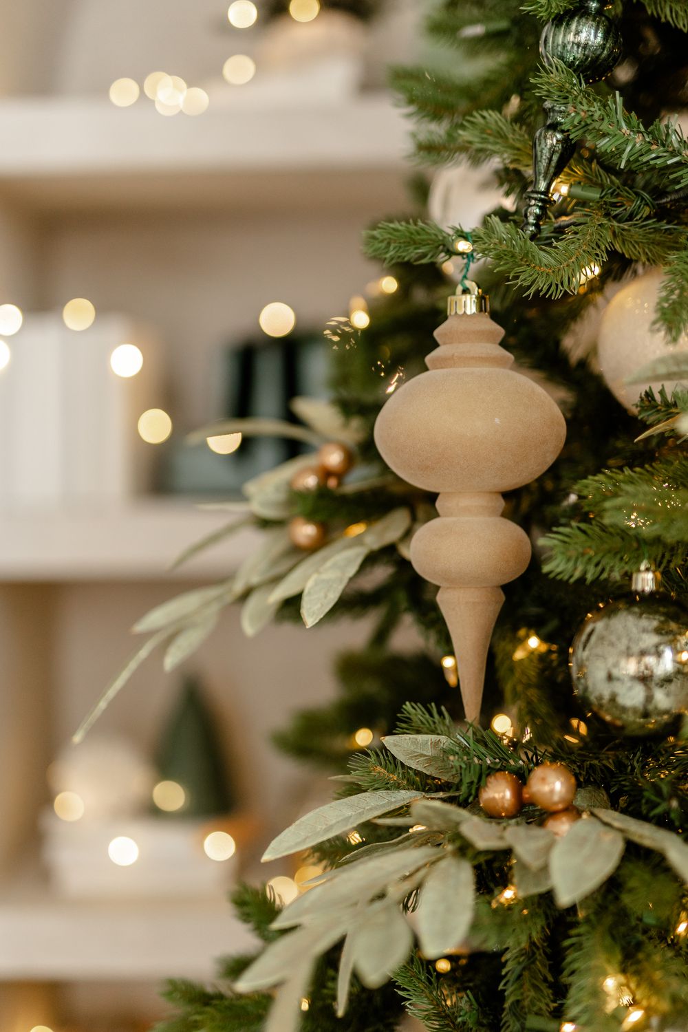 Close-up of wooden finial ornament and greenery on Christmas tree with bokeh lights in background.