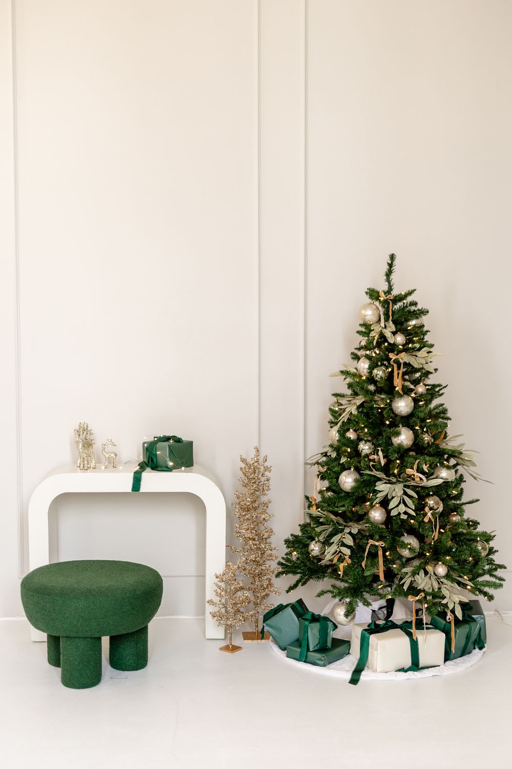 Minimalist green Christmas scene with small trees and wrapped presents against a white wall.