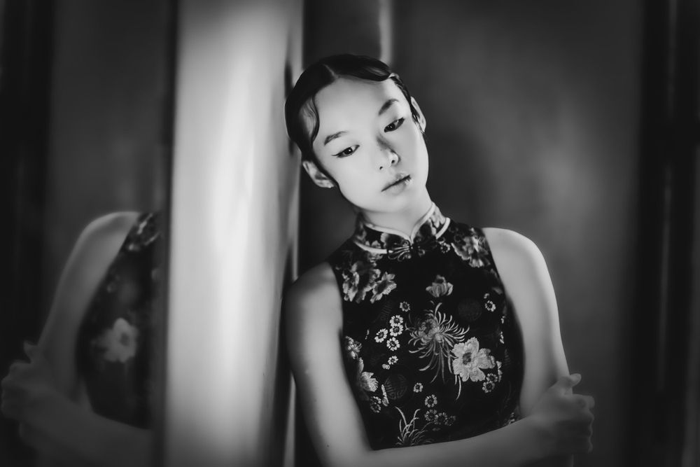 Atmospheric black and white portrait of a woman in traditional Chinese qipao dress with floral embroidery.